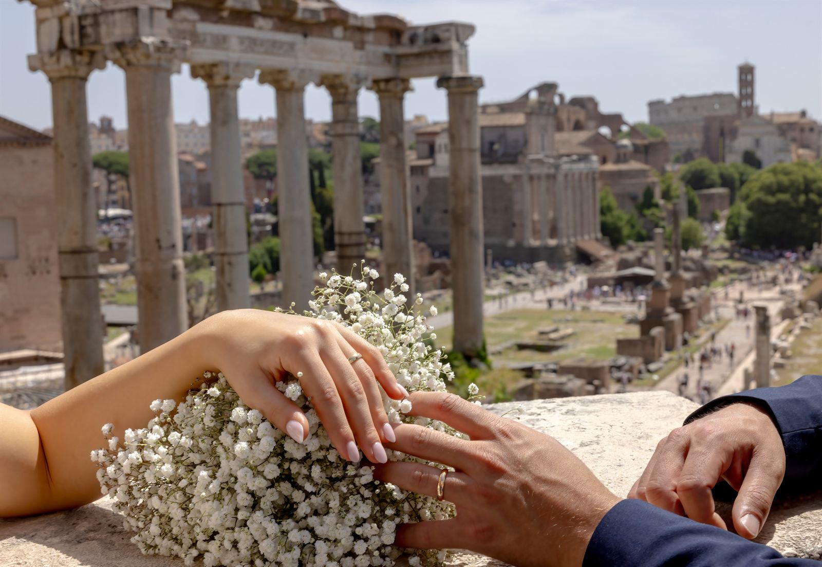Mani degli sposi con le fedi e il bouquet, sullo sfondo il Foro Romano